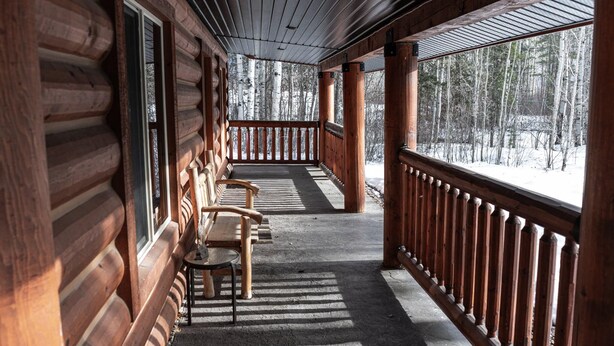 A wooden cabin with a covered porch, wooden benches, and a view of a snowy forest. - Legacy Vacation Rental - Pet Friendly! (Valemount)