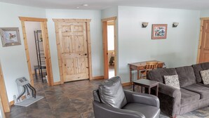 A living room with a leather armchair, a sofa, a wooden door, a dining table with chairs, and a small heater on the floor. - Legacy Vacation Rental - Pet Friendly! (Valemount)
