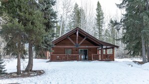 A log cabin with a porch, surrounded by snow and tall evergreen trees. - Legacy Vacation Rental - Pet Friendly! (Valemount)
