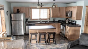 A kitchen with wooden cabinets, a stainless steel refrigerator, a microwave, and a stove. There are stools at the island and a dining table with chairs. - Legacy Vacation Rental - Pet Friendly! (Valemount)