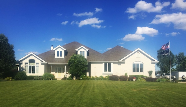 A large, single-story house with a well-maintained lawn, a garage, and an American flag.