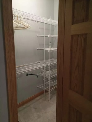 A closet with multiple shelves and a hanging rod, containing a bottle and a hanger.