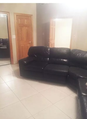 A living room with a black leather sofa, a wooden door, and a tiled floor.