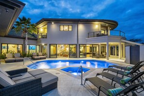 A modern two-story house with a swimming pool, outdoor seating, and a well-lit patio area.
