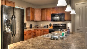 A kitchen with wooden cabinets, a stainless steel refrigerator, a microwave, and a granite countertop. - Believe N Dreams #317 – Your Peaceful Retreat in the Heart of Pigeon Forge (Pigeon Forge)