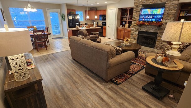 A modern living room with a sofa, a coffee table, and a fireplace. There is a kitchen in the background with wooden cabinets and a stone accent wall. - Believe N Dreams #317 – Your Peaceful Retreat in the Heart of Pigeon Forge (Pigeon Forge)