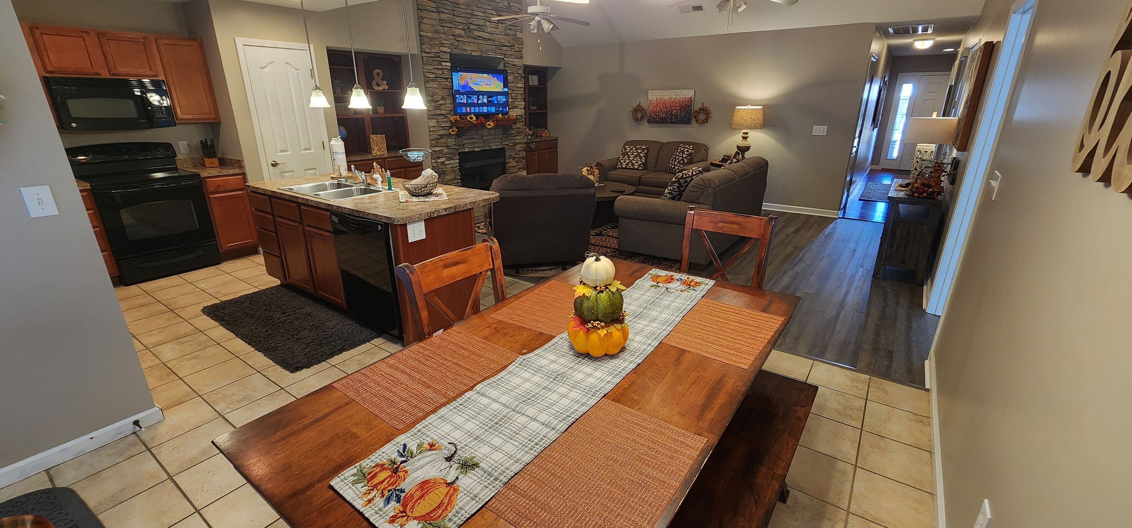 Una cocina moderna con una isla central, un comedor con una mesa preparada para cuatro personas y una sala de estar con sofá y chimenea.