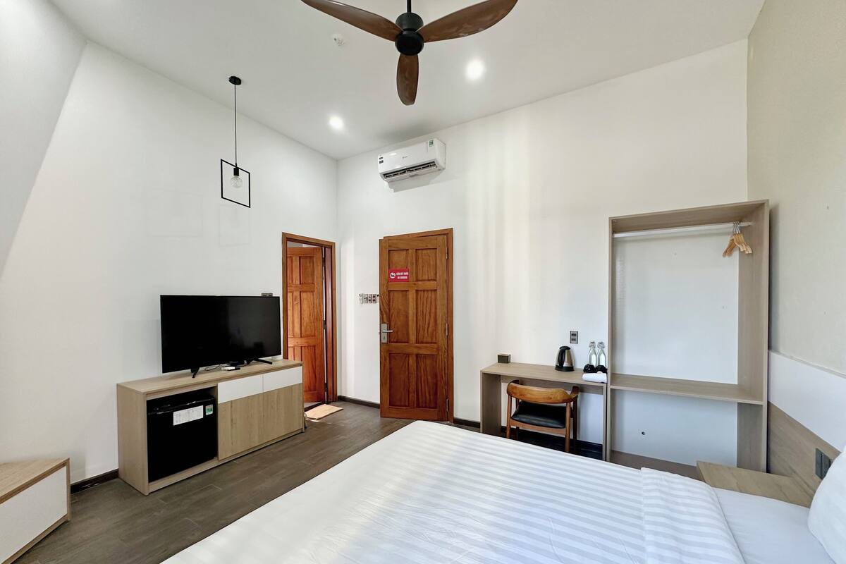 A hotel room with a bed, a desk, a television, a ceiling fan, and an air conditioning unit.