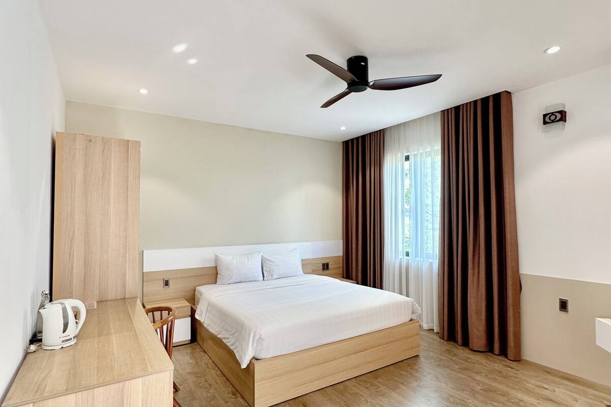 A modern hotel room with a wooden bed, a desk, a ceiling fan, and a window with curtains.