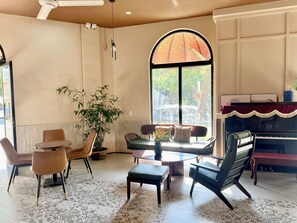 A room with a piano, seating area, and a large window with a view of trees. - Soleil House Hostel (Hue)