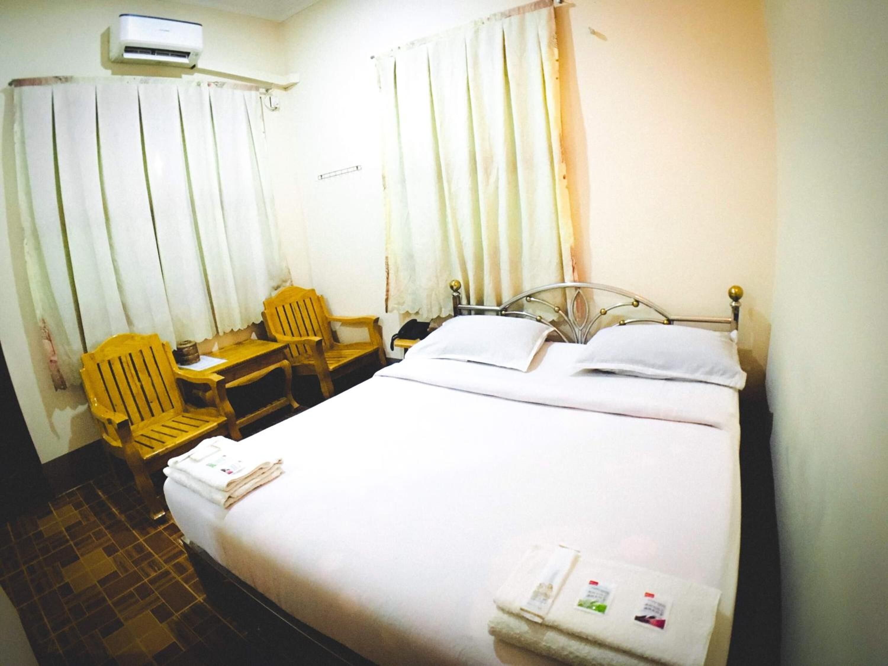 A hotel room with a bed, a desk with a chair, a small table, and an air conditioning unit.
