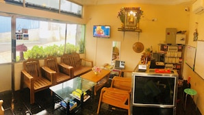 A room with wooden chairs, a glass table, a TV, a computer, and a small altar with flowers. - Pinlon Pann motel (Mawlamyine)