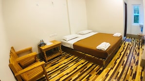 A hotel room with a wooden floor, a bed with white linens, a wooden chair, a small table with a water bottle, and a window. - Pinlon Pann motel (Mawlamyine)