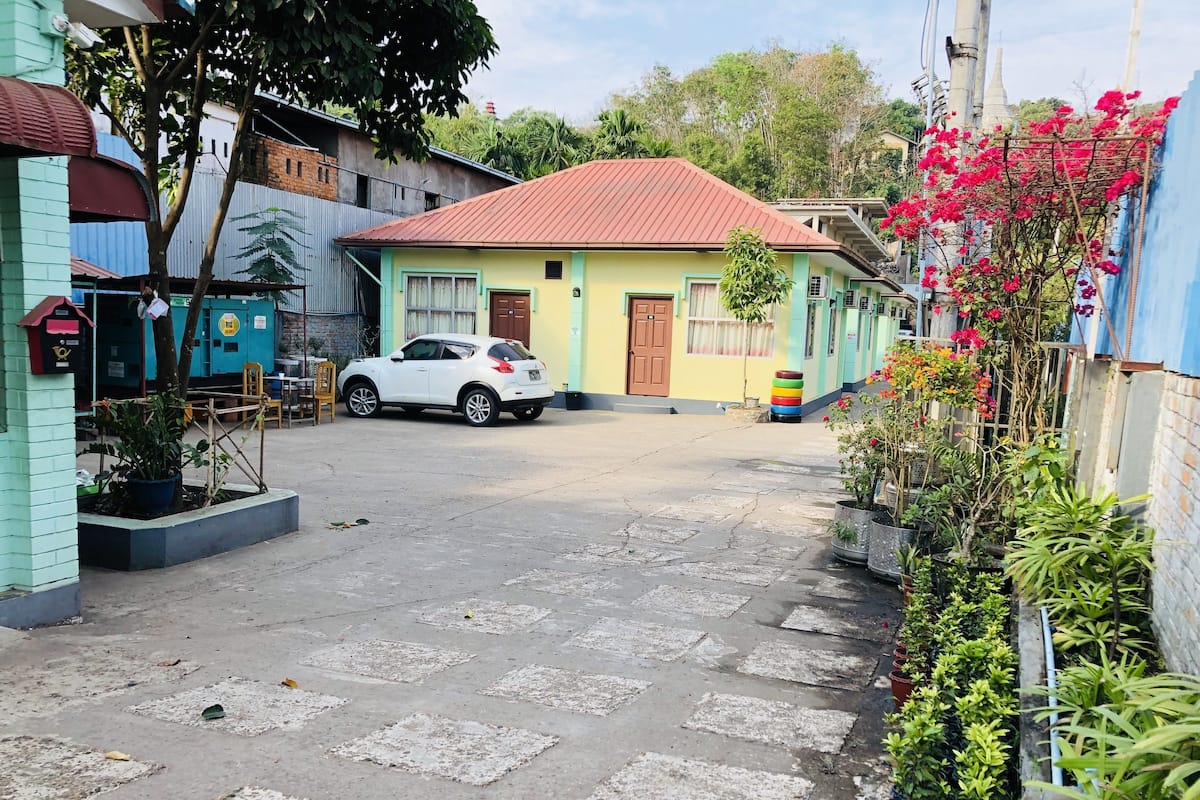 A courtyard with a white car parked in the center, surrounded by buildings with colorful facades and potted plants.
