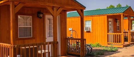 A wooden cabin with a porch, a bicycle, and a green roof.