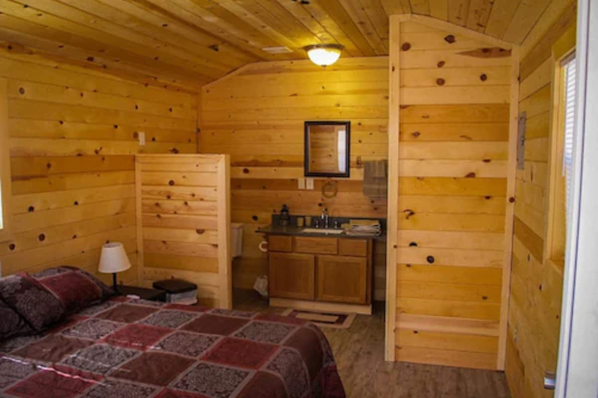 A cozy wooden cabin room with a bed, a small desk, and a kitchenette.