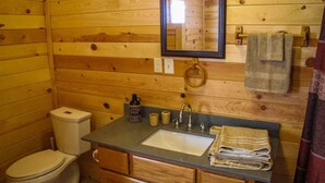 A wooden cabin bathroom with a toilet, sink, and wooden cabinets. - Zion's Cozy Cabins (Hildale)