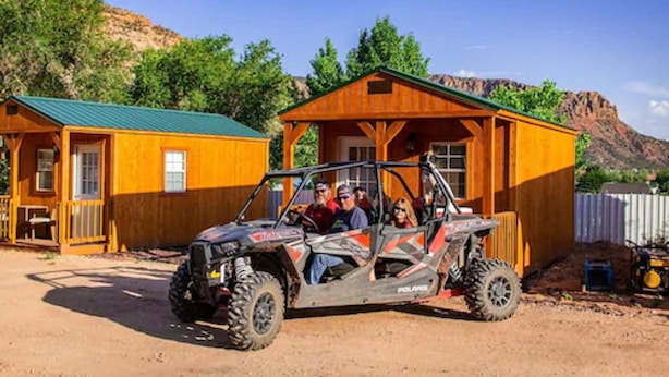 A wooden cabin with a green roof, a dirt driveway, and a mountain in the background. - Zion's Cozy Cabins (Hildale)