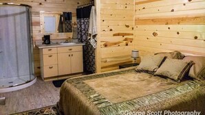 A wooden cabin room with a bed, a sink, and a shower. - Zion's Cozy Cabins (Hildale)