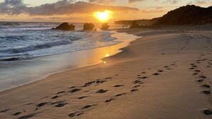 Ein Strand mit Fußspuren, die zum Meer führen, unter einem klaren Himmel bei untergehender Sonne.