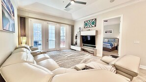 A spacious living room with a large sectional sofa, a flat-screen TV, and a ceiling fan. - Immaculate Family Friendly 3BR/3BA  Beach Villa with TESLA Charger (Amelia Island)