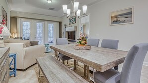 A dining area with a wooden table, grey chairs, and a bench. There is a chandelier above the table and a painting on the wall. - Immaculate Family Friendly 3BR/3BA  Beach Villa with TESLA Charger (Amelia Island)