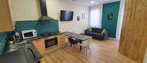 Una cucina moderna con microonde, piano cottura e lavello. C'è una zona pranzo con tavolo e sedie. Un televisore è montato a parete e un divano si trova nell'area living.