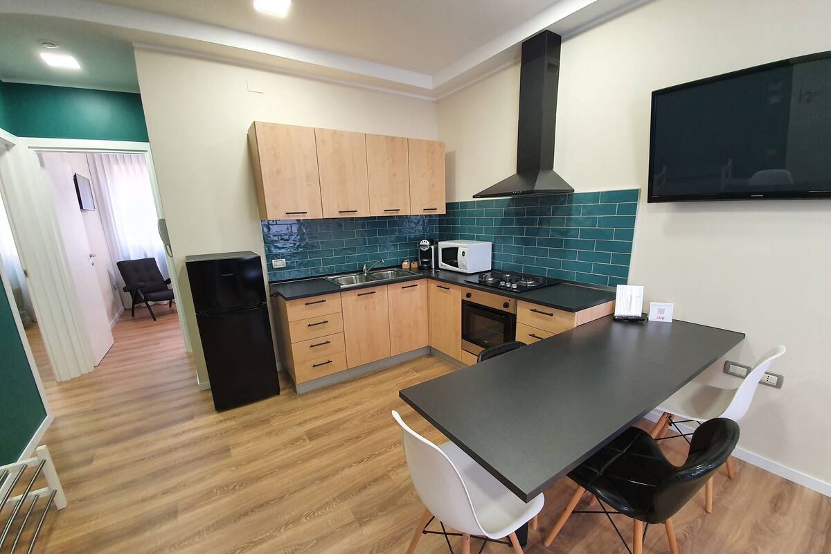 A compact kitchen with wooden cabinets, a black stove, and a dining area with two chairs.