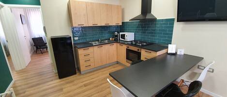 A compact kitchen with wooden cabinets, a black stove, and a dining area with two chairs.