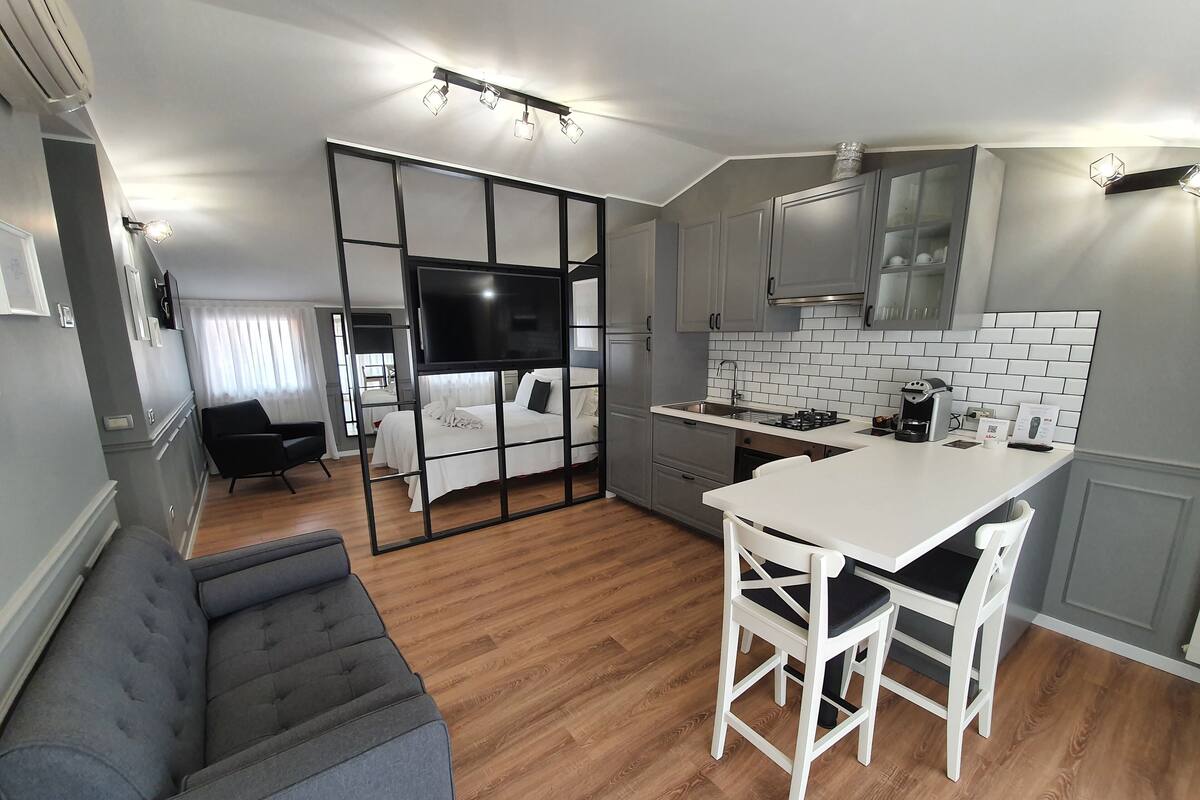 A modern kitchen with a dining area, a sofa, and a TV in the background.