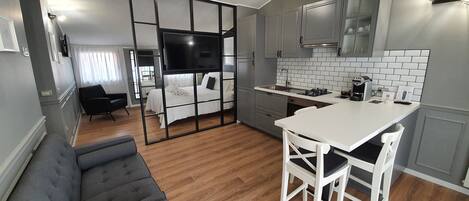 A modern kitchen with a dining area, a sofa, and a TV in the background.