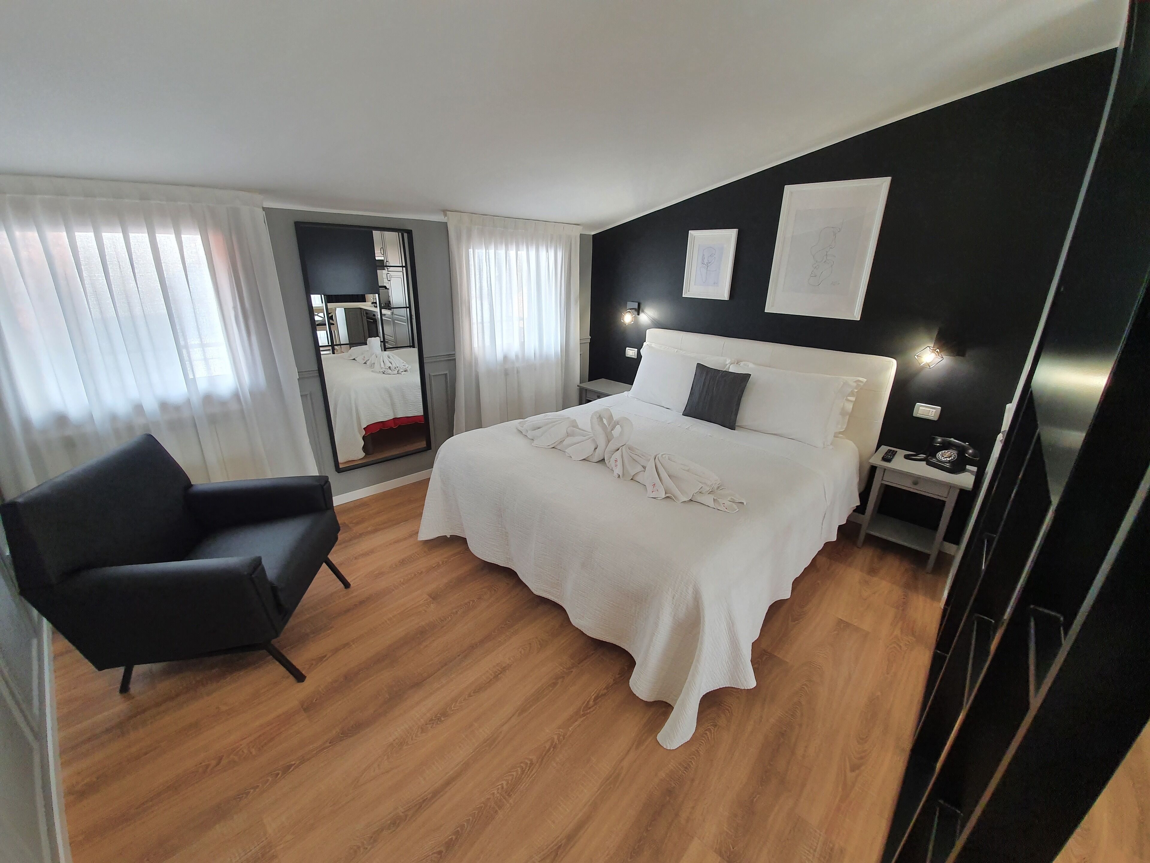 A hotel room with a bed, a chair, a bedside table, and a mirror.