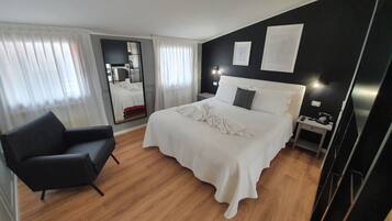 A hotel room with a bed, a chair, a bedside table, and a mirror.