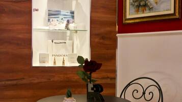 A wooden wall with a framed picture, a glass display case with luxury items, and a small table with a rose.