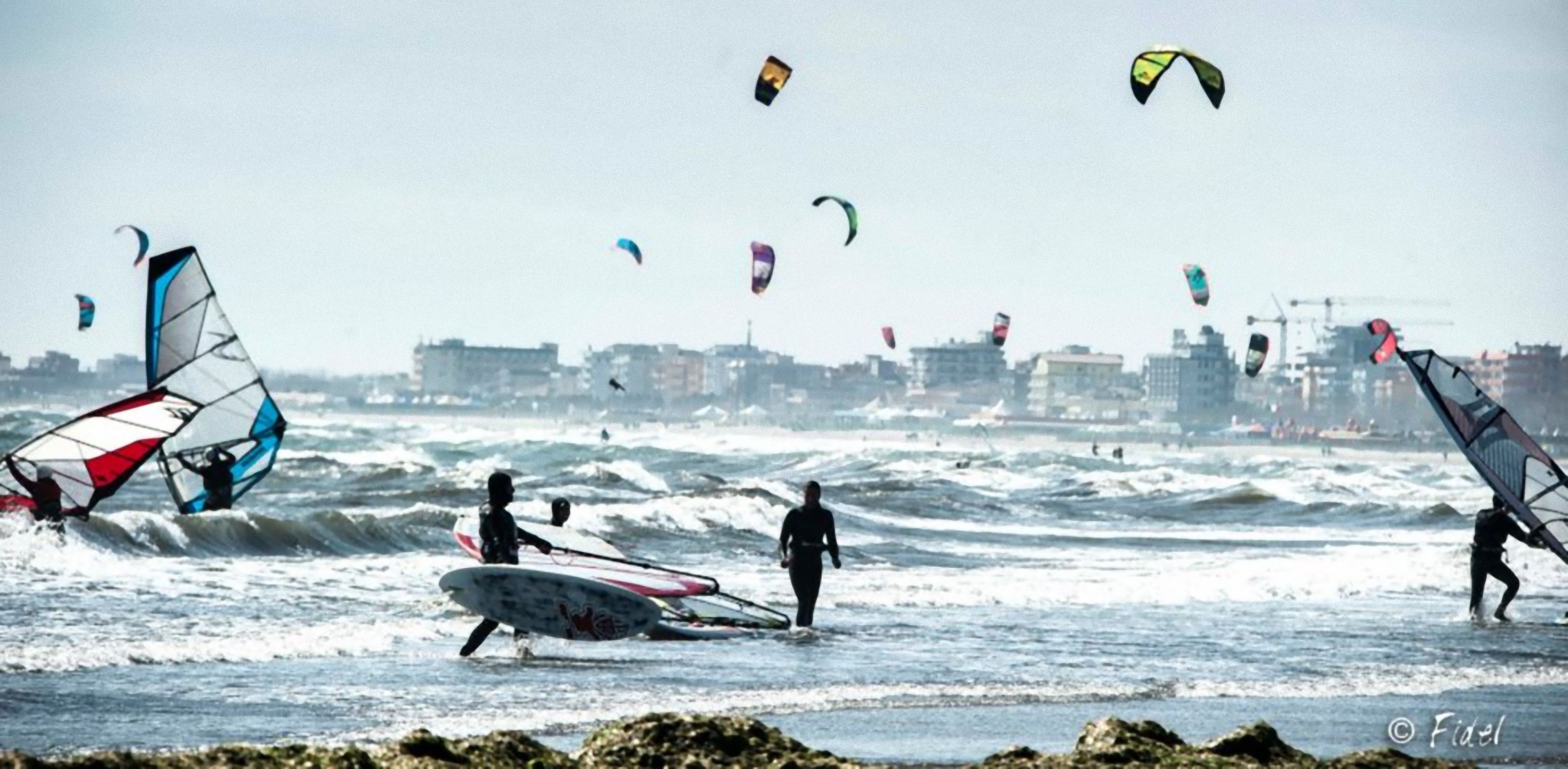 A beach with people windsurfing and kite surfing.