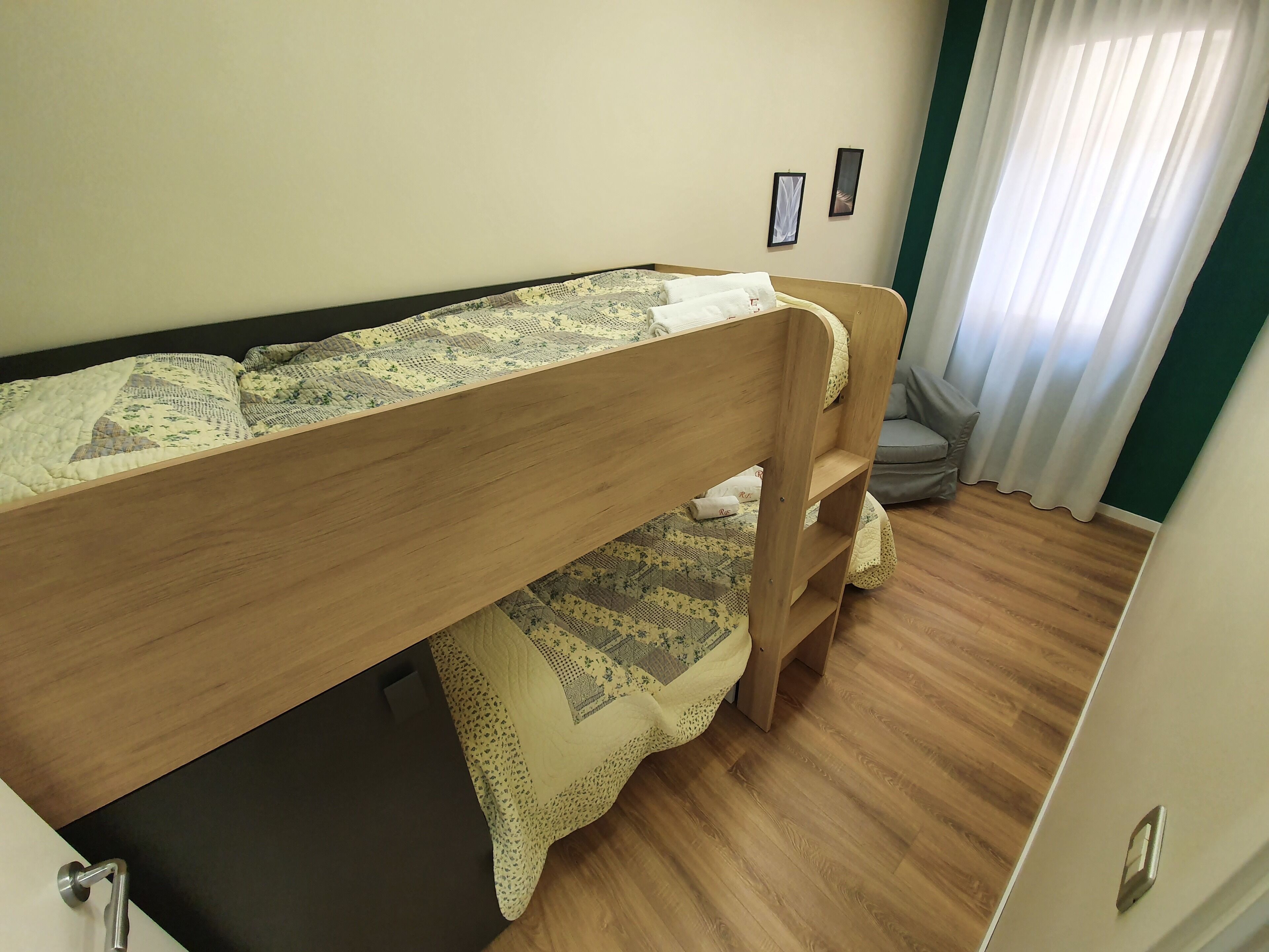 Una cama litera con colcha acolchada, suelo de madera y ventana con cortinas.