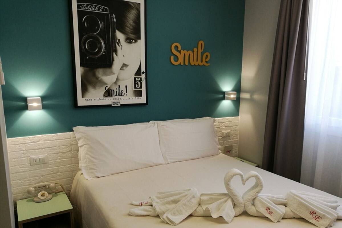 A hotel room with a bed, a wall-mounted poster, and a bedside table with a telephone.