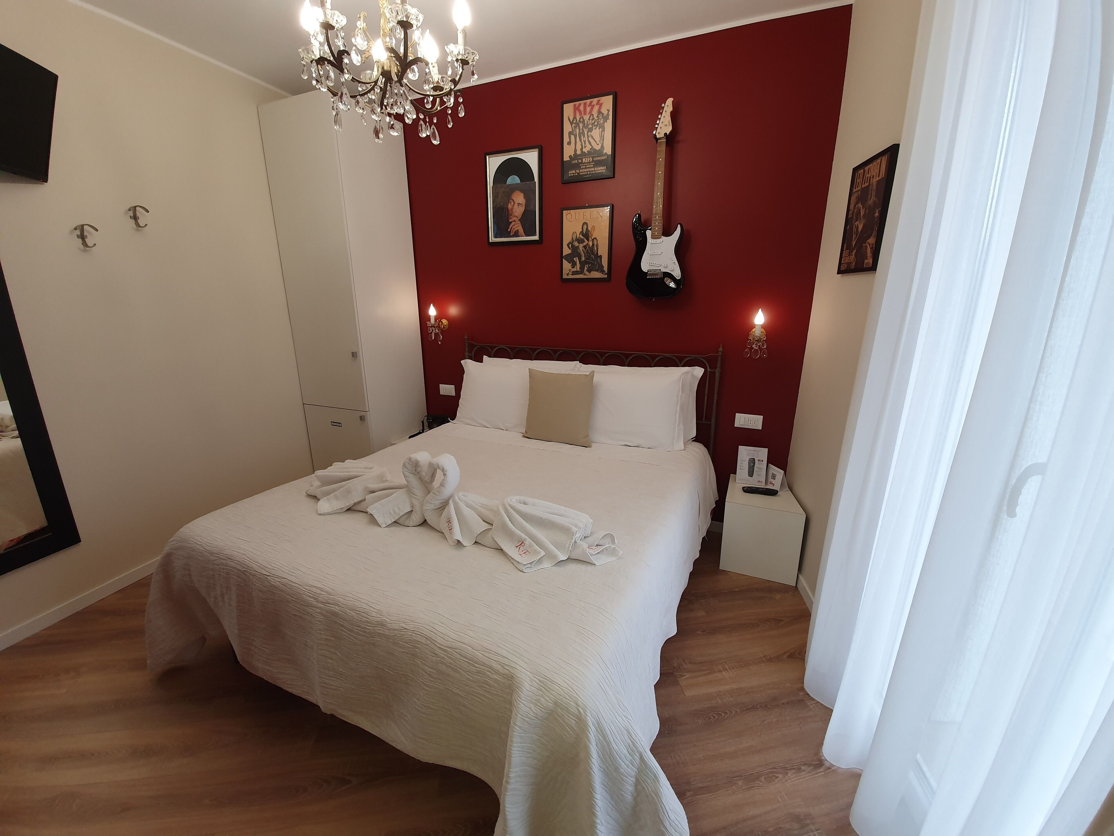 A hotel room with a bed, a chandelier, a guitar, and a red wall.