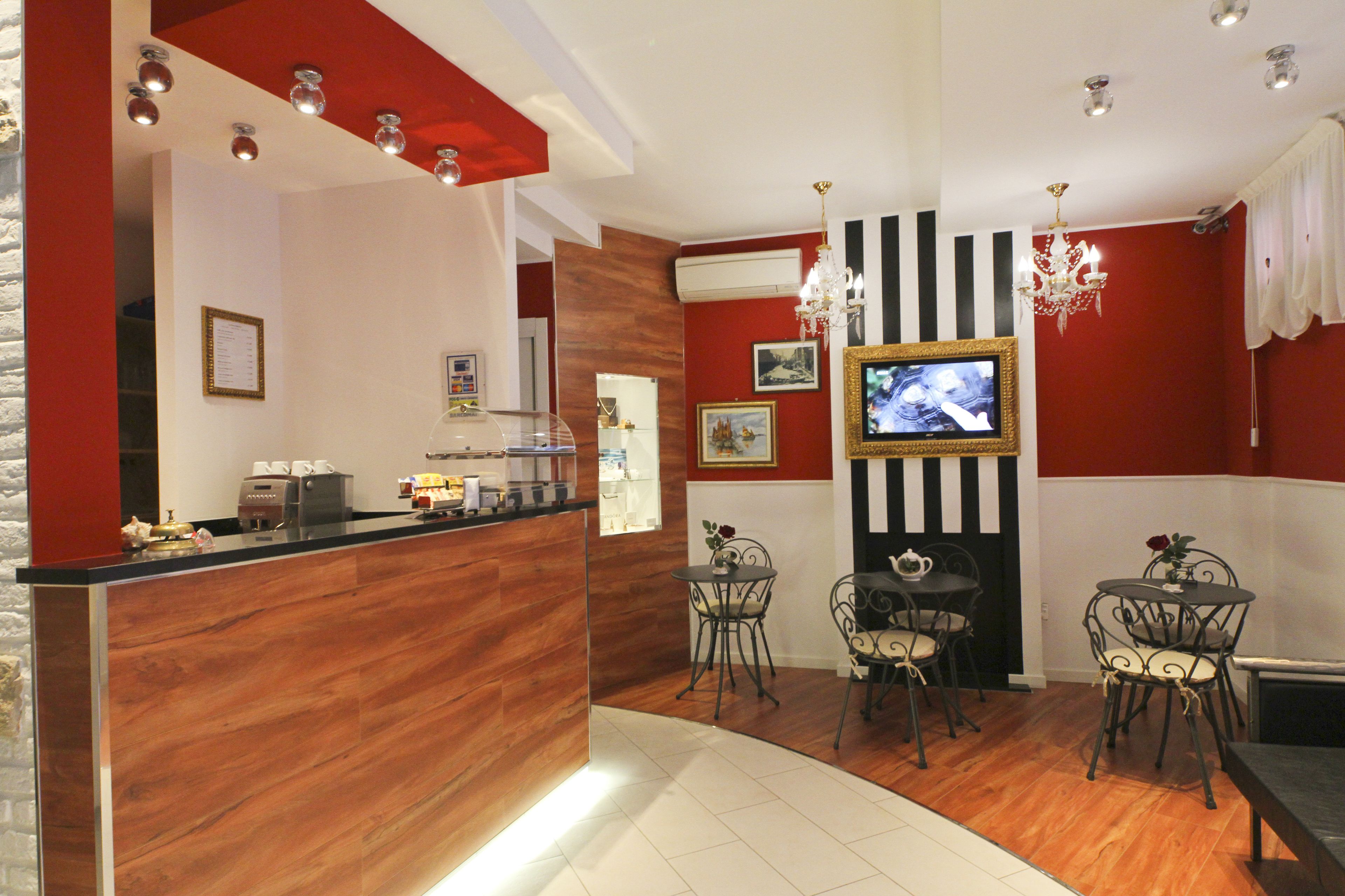 A modern hotel lobby with a wooden reception desk, a television mounted on the wall, and a seating area with metal chairs.