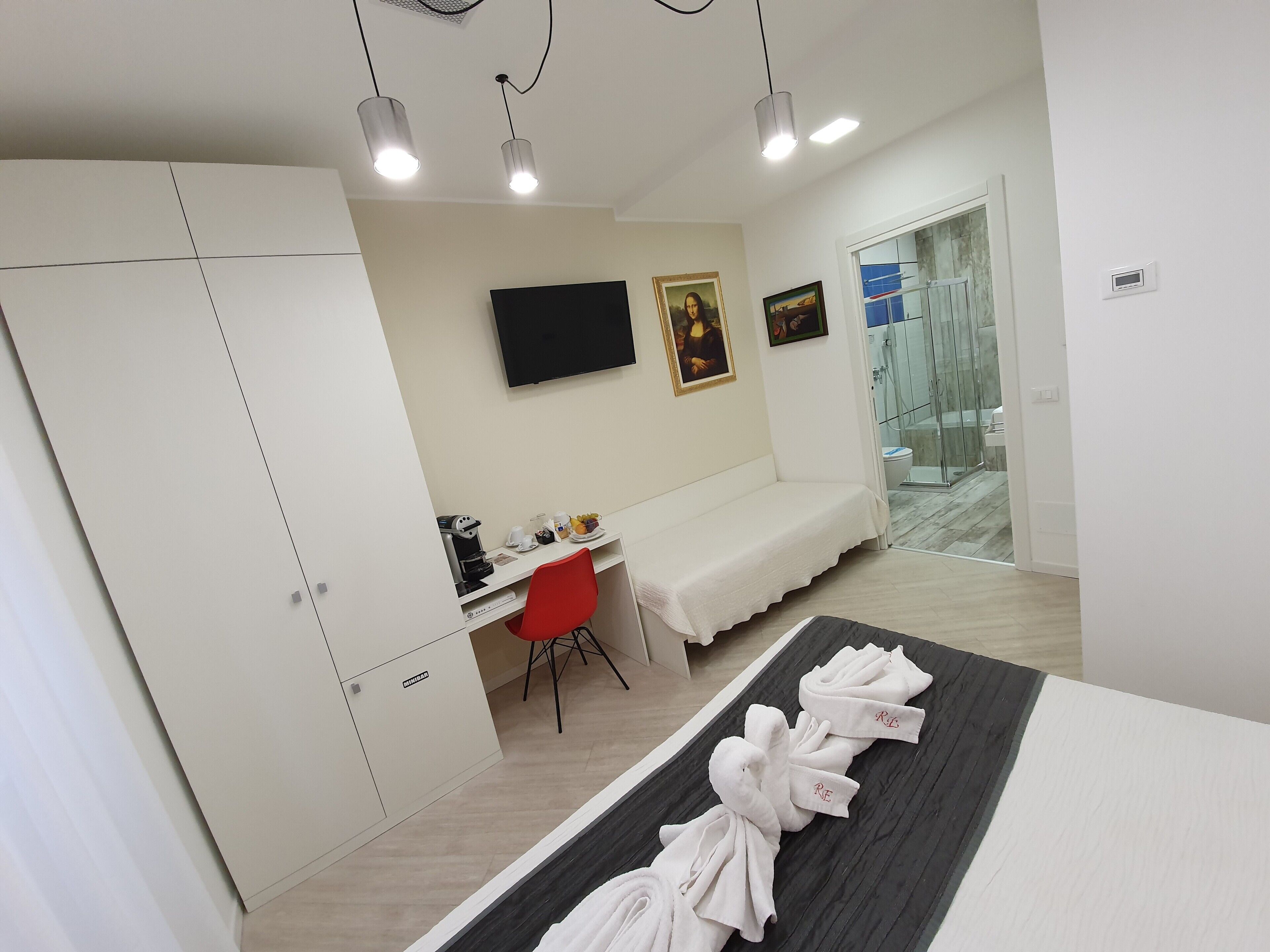 A hotel room with a bed, a desk, a chair, a TV, and a shower area.