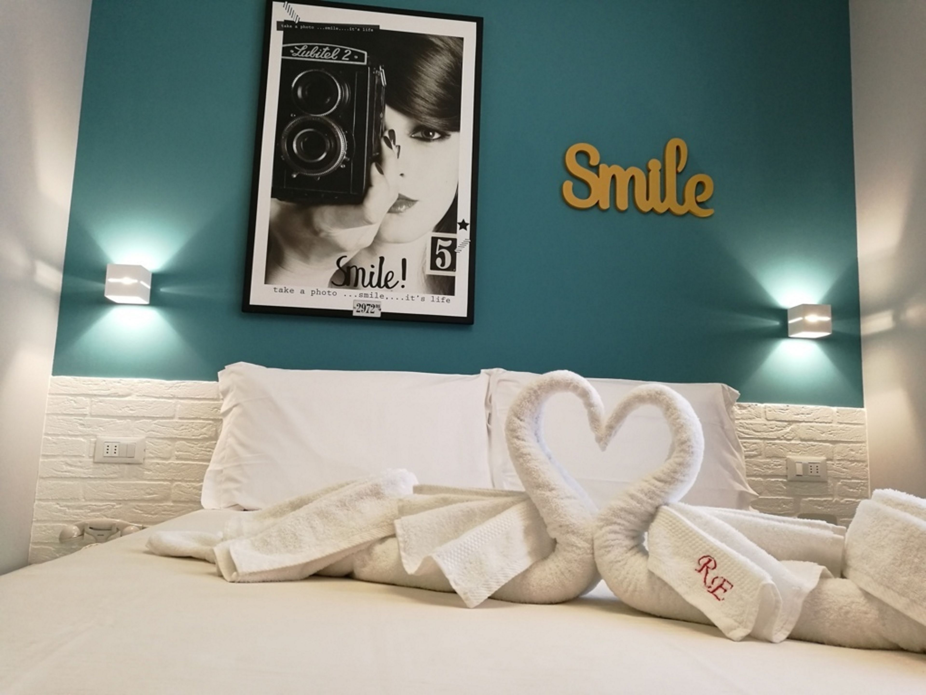 Ett hotellrum med en turkosfärgad accentvägg, ett inramat foto av en kamera och en skylt med texten ”Le”.