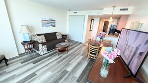 Una sala moderna con sofá, mesa de centro y mesa de comedor. Hay un televisor sobre un mueble bajo y un florero con flores en la mesa.