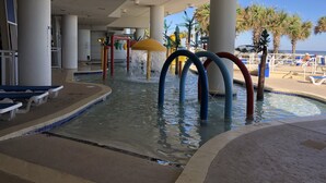 Un área de piscina con fuentes, sillones de descanso y palmeras.