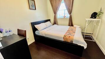A hotel room with a bed, a desk, a chair, a small table, a window with curtains, and a wall-mounted picture.