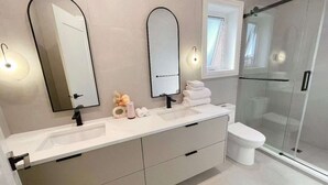 Un baño moderno con tocador doble, dos espejos en la pared, inodoro y cabina de ducha con mampara de cristal.