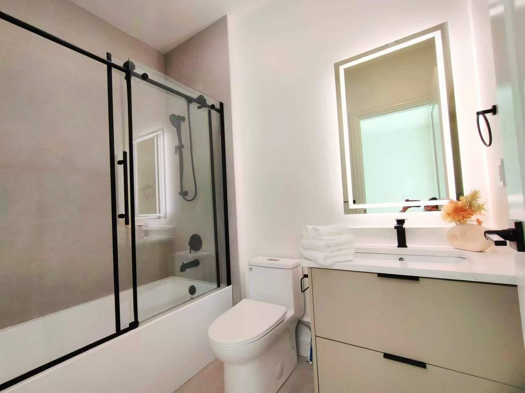 Een moderne badkamer met een douchecabine van glas, een wit toilet en een wastafel met spiegel.