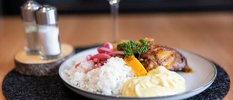 A plate of food with rice, a meat dish, and a side of sauce, accompanied by a glass of wine and salt and pepper shakers on a wooden table.
