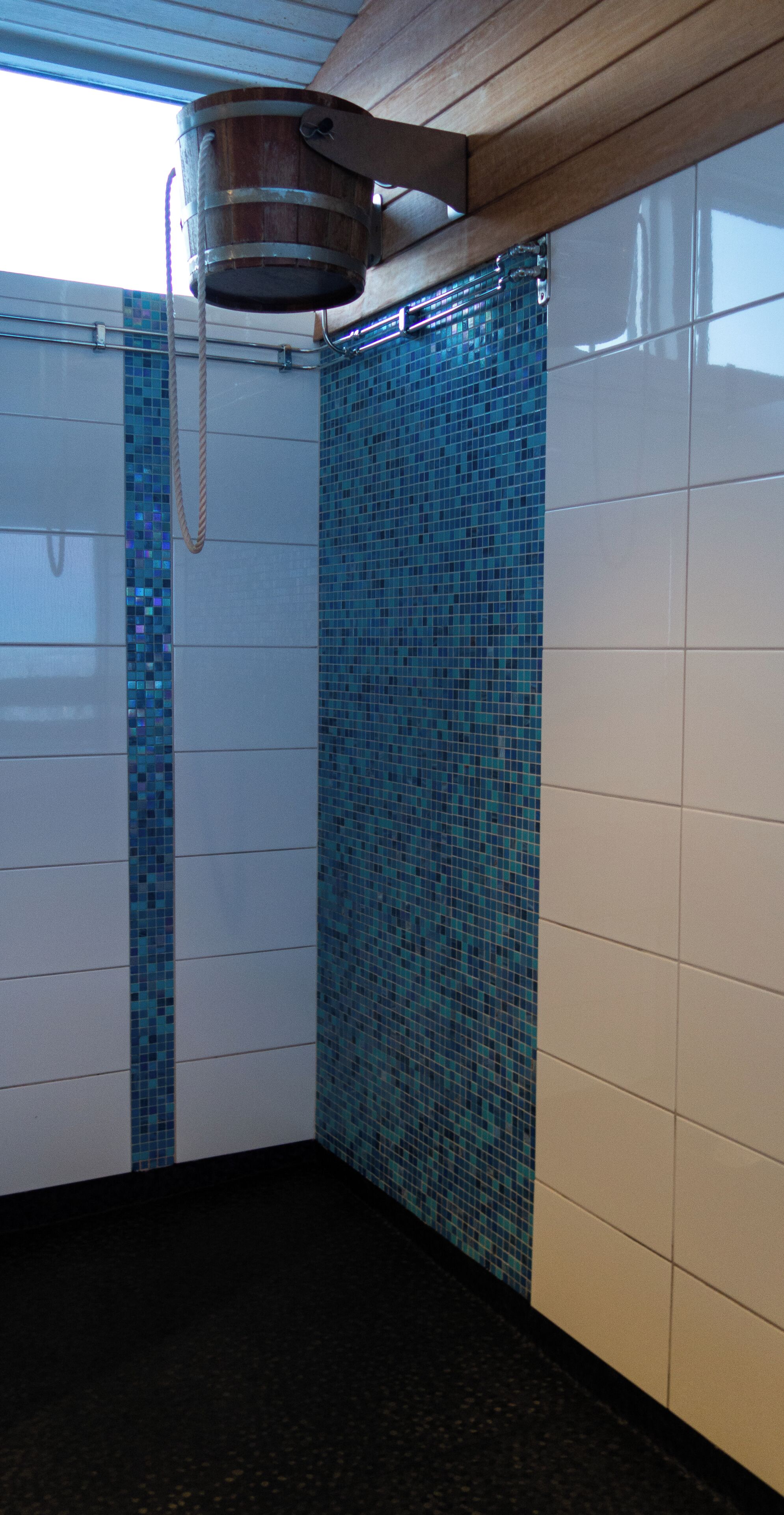A shower with a wooden ceiling, tiled walls, and a metal bucket.