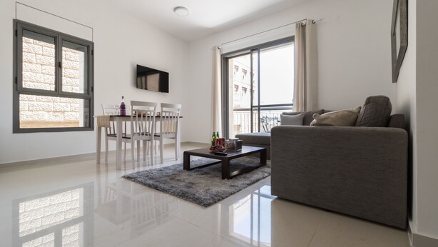 A modern living room with a grey sofa, a coffee table, and a dining area with chairs and a table. - Yafo 35 - Isrentals (Jerusalem)