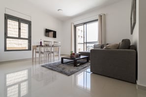 A modern living room with a grey sofa, a coffee table, and a dining area with chairs and a table. - Yafo 35 - Isrentals (Jerusalem)